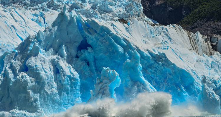 Gros plan d'un mur de glacier bleu éclatant qui vêle avec des éclaboussures d'eau glacée au premier plan