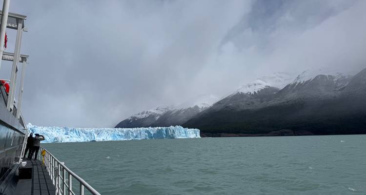 Een bootpassagier fotografeert de rand van gletser Perito Moreno vanuit een winderig turquoise meer.