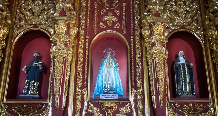 Retable d'église doré orné avec trois statues religieuses sur fond rouge profond.
