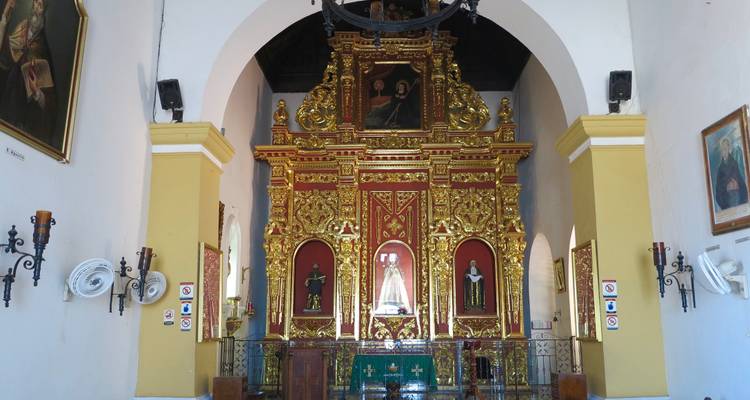 Intérieur d'une petite chapelle avec un autel doré richement décoré encadré par des murs blancs et des arches.