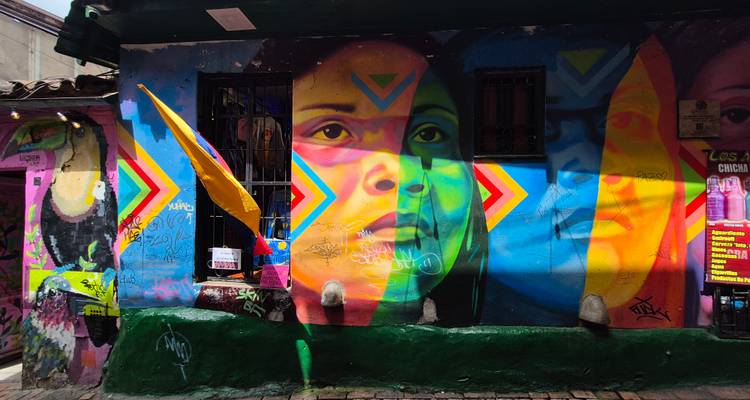 Fresque murale de rue multicolore éclatante représentant des visages superposés avec des motifs de flèches géométriques sur un mur urbain.