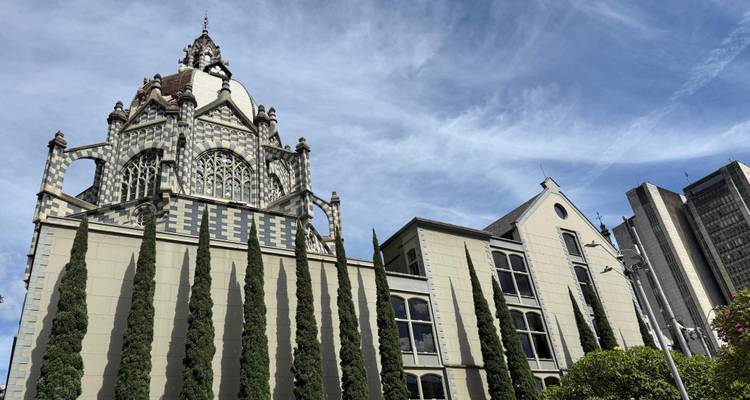 Palacio neogótico distintivo con patrones en blanco y negro flanqueado por altos cipreses bajo un cielo rayado.