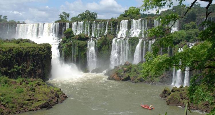 Les vastes chutes d'Iguazú se déversant dans une gorge tandis qu'un petit radeau navigue sur la rivière tumultueuse en contrebas.