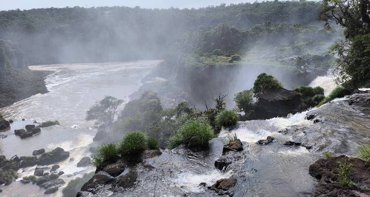 Vue brumeuse depuis le sommet des chutes d'Iguazú avec des embruns qui s'élèvent et des collines de jungle en arrière-plan.
