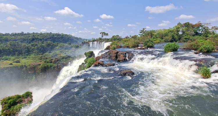 Uitzicht vanaf de top van de Iguazú Falls met mist die opstijgt in een helderblauwe lucht.