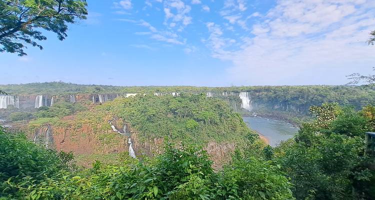Uitgebreid uitzicht over weelderig groen en een lange gordijn van de Iguazú-watervallen onder een blauwe hemel.