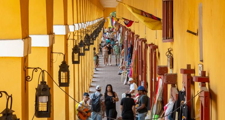 Bullicioso corredor interior de Las Bóvedas con paredes amarillo brillante, faroles y puestos de souvenirs abarrotados de compradores.