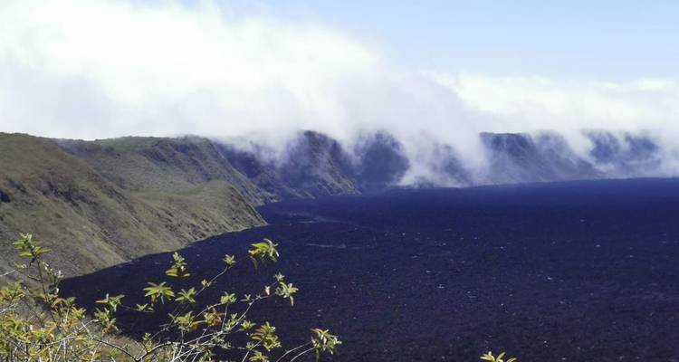 El suelo oscuro de la caldera volcánica contrasta con la capa de nubes brumosas que se derrama sobre el borde del cráter.