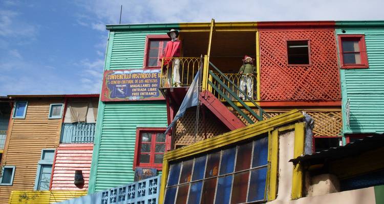 Bâtiments en bois aux couleurs vives et mannequins sur un balcon dans un barrio coloré.