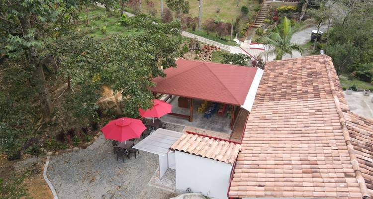 Foto aérea oblicua de una casa de campo con tejado de tejas, patio y sombrillas rojas junto a los árboles.