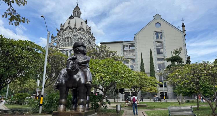 Eine bronzene Botero-Reiterstatue steht vor dem gemusterten Palacio de la Cultura und gepflegten Gärten.