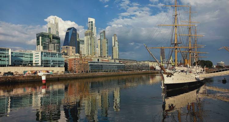 Skyline moderne de Puerto Madero reflété dans le canal avec un grand voilier historique amarré au premier plan.