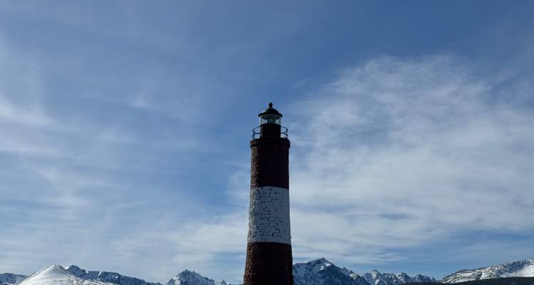 Iconische rood-witte vuurtoren staat afgetekend tegen een achtergrond van sneeuwbergen en sluierige wolken.