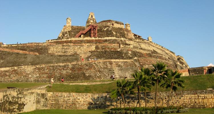 Des visiteurs gravissant les murs en terrasses de l'historique Castillo San Felipe dans la douce lumière du soir.