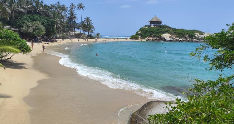 Plage emblématique de Cabo San Juan avec une eau cristalline, des nageurs et une hutte au toit de chaume au sommet de la colline dans le parc national de Tayrona.