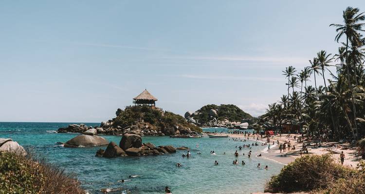 Petite crique animée des Caraïbes au parc national de Tayrona avec ses eaux turquoise, ses baigneurs et son petit belvédère coiffé de palmiers.