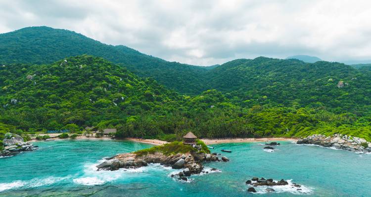 Vue aérienne des montagnes luxuriantes couvertes de jungle rencontrant une baie en croissant d'une mer turquoise cristalline à Tayrona.