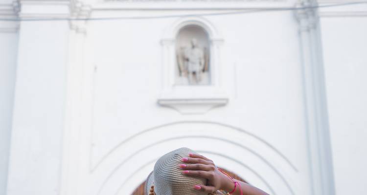 Close-up of a traveler holding a straw hat against a white colonial church façade.