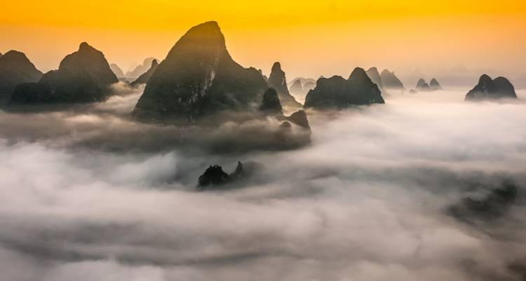 Montagnes karstiques spectaculaires émergeant des nuages au lever du soleil.