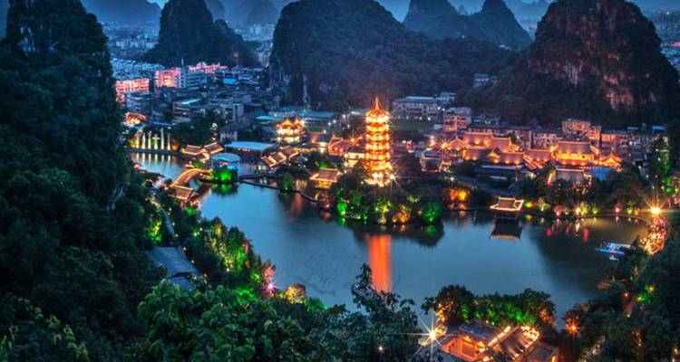 Vue nocturne d'une pagode vivement éclairée et d'une rivière dans un paysage urbain.