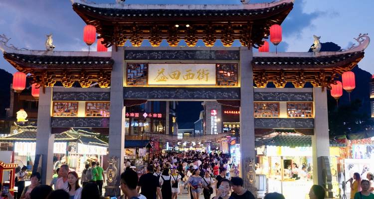 Un marché de rue animé avec une arche décorative la nuit.