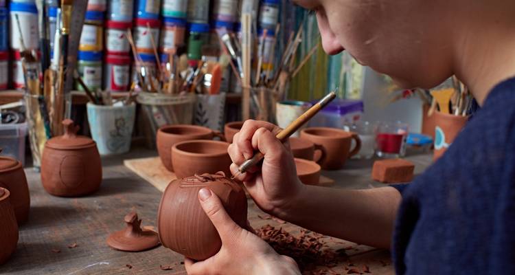 Een persoon die aardewerk maakt aan een werkbank.