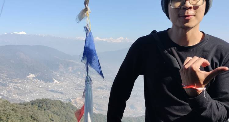 Personne posant avec des drapeaux de prière et vue sur les montagnes.