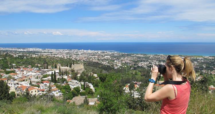 Woman photographing a coastal city with a historic building.