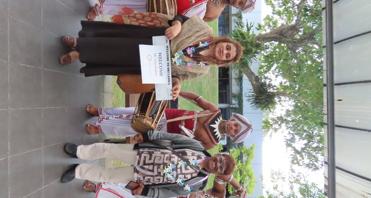 Grupo de personas con ropa tradicional sosteniendo un cartel de bienvenida.