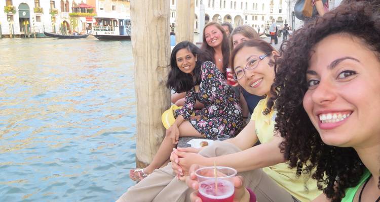 Groupe d'amis assis au bord d'un canal vénitien en train de savourer des boissons.