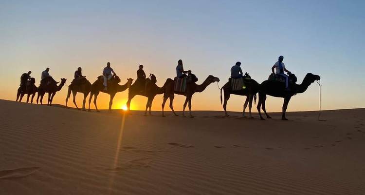 Silhouette de caravane de chameaux avec cavaliers traversant une dune du désert au lever du soleil avec un soleil éclatant.
