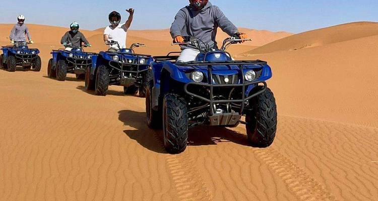 Groupe de conducteurs pilotant des quads bleus à travers le sable ondulé du désert en laissant des traces.