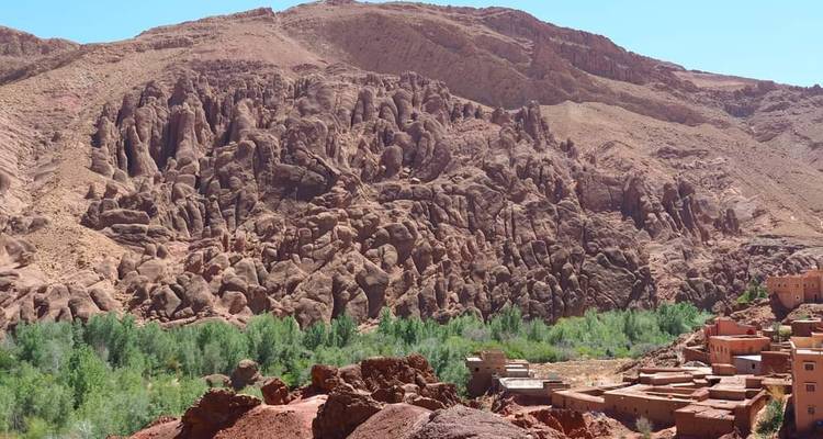 Des formations rocheuses rougeâtres et escarpées s'élevant au-dessus d'un village oasis verdoyant au fond de la vallée dans les Gorges du Dadès.