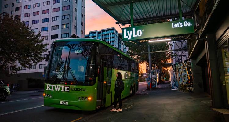 Stadsstraatscène met een bus geparkeerd onder een luifel van een gebouw bij zonsondergang.
