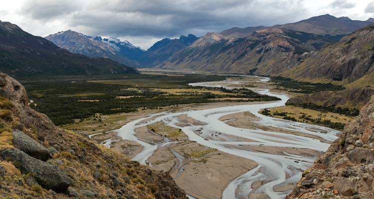 Vaste vallée patagonienne avec une rivière en tresses serpentant vers des pics enneigés au loin