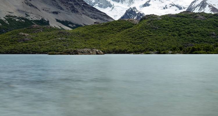 Lac tranquille avec des pentes boisées et des sommets enneigés à moitié obscurcis par la brume en arrière-plan