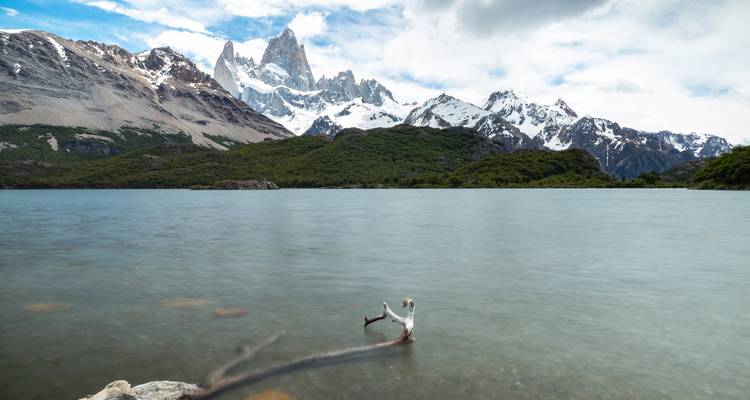 L'iconique mont Fitz Roy se reflétant dans un lac calme avec du bois flotté au premier plan et des nuages dramatiques