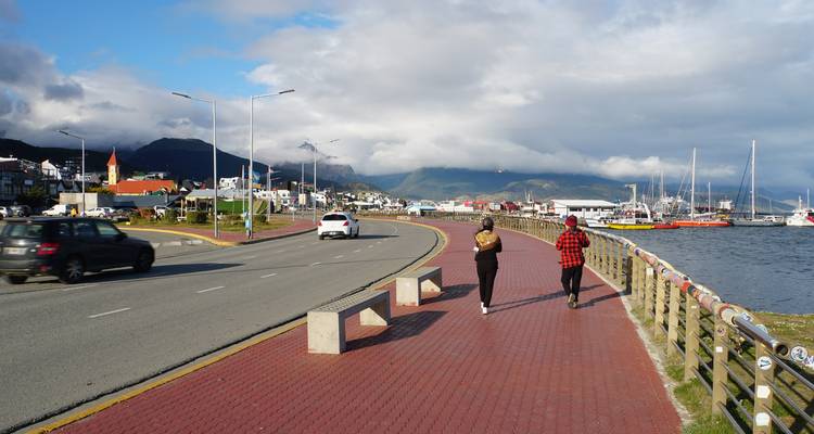 Deux jeunes gens se promènent le long d'une promenade en briques rouges à côté de la route du front de mer et de la marina à Ushuaia.