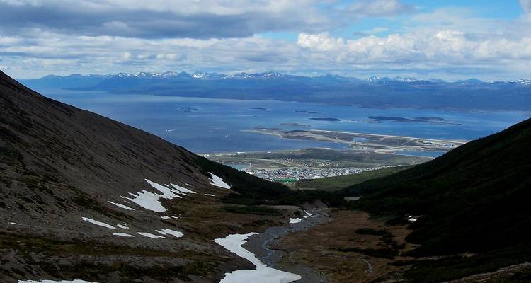 Vue en altitude sur une vallée aride vers le canal Beagle et les chaînes de montagnes lointaines.