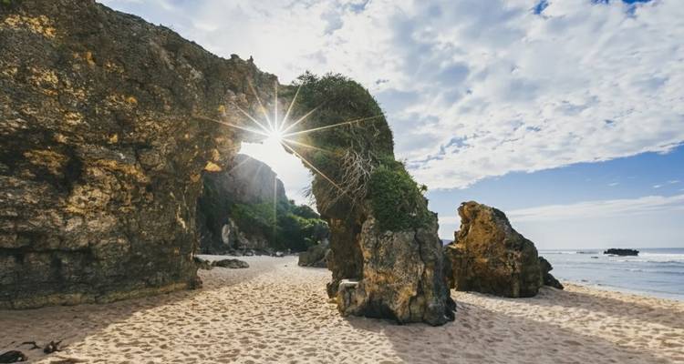 La lumière du soleil filtrant à travers une arche rocheuse naturelle sur une plage de sable.