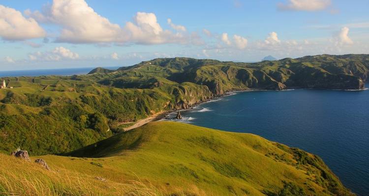 Vue panoramique de collines vertes et d'un littoral océanique bleu.