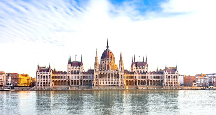 Le bâtiment du Parlement hongrois se reflétant dans le Danube sous un ciel lumineux.