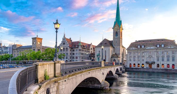 Pont de pierre historique et flèche d'église au-dessus de la rivière Limmat à Zurich au coucher du soleil.