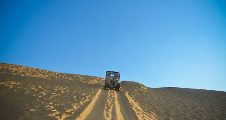 Ein Jeep, der eine Sanddüne unter einem klaren blauen Himmel hinaufführt.