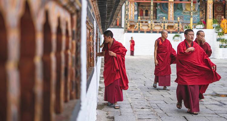 Monks in red robes walking through a temple courtyard.