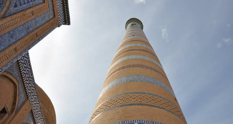 A towering brick minaret with decorative bands viewed from below.