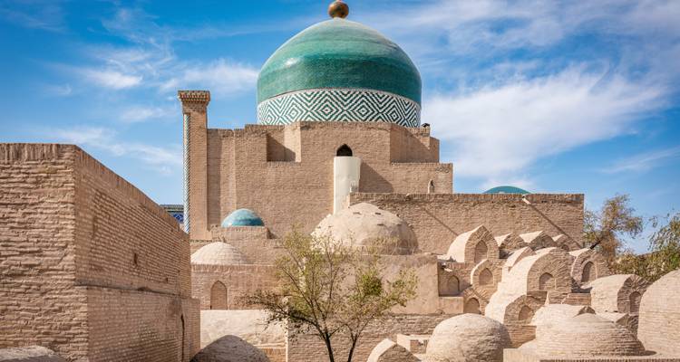 Grand dôme turquoise s'élevant au-dessus de mausolées en briques de terre sous un ciel partiellement nuageux
