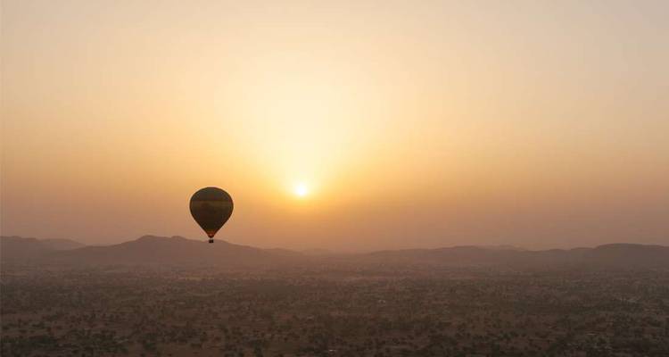Une montgolfière au lever du soleil au-dessus d'un vaste paysage.