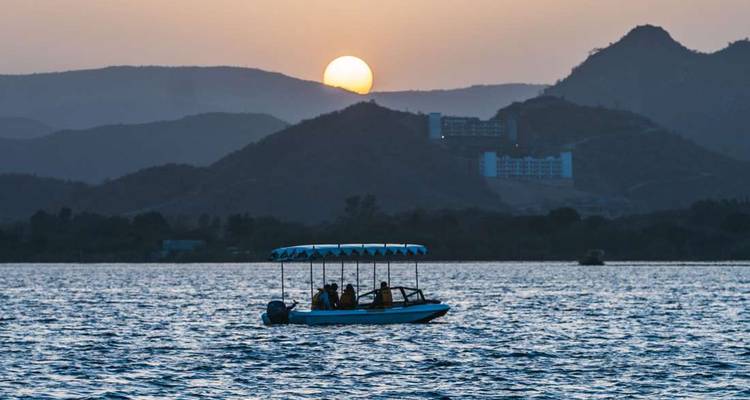 Un bateau sur un lac au coucher du soleil avec des montagnes en arrière-plan.