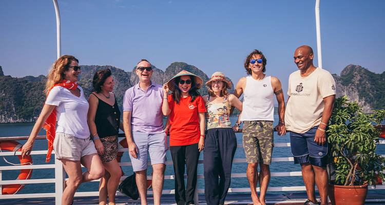 Grupo de amigos posando en la cubierta de un barco con acantilados de piedra caliza al fondo.